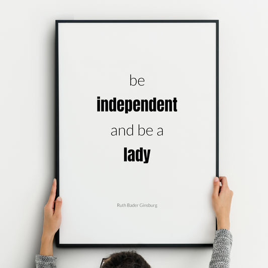 Single portrait typography print. Text reads: Be independent and be a lady. An attribution to Ruth Bader Ginsburg is below. "Independent lady" is highlighted in bold. Text is in a lower case sans serif font, black on a white background.