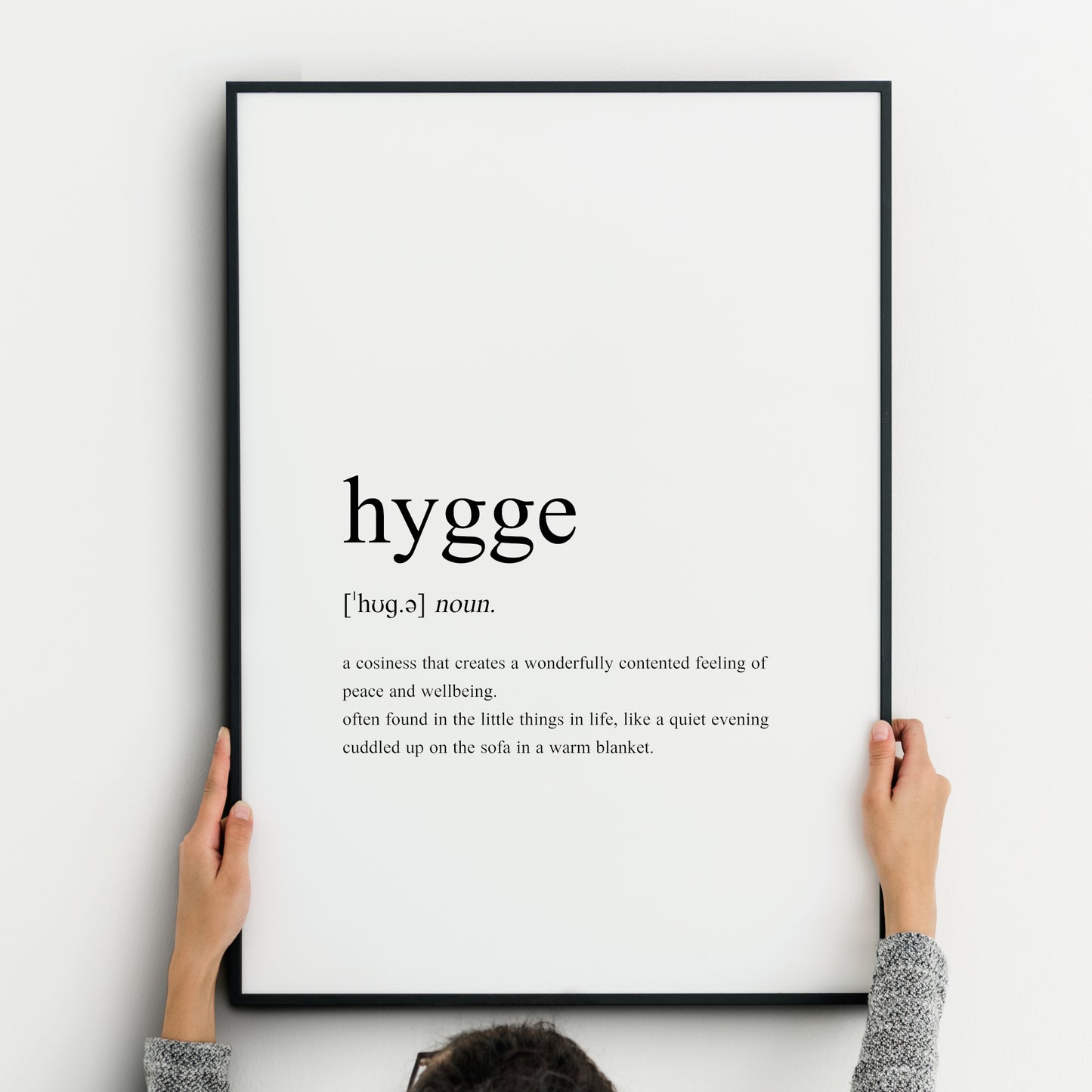 Single portrait typography print featuring a dictionary-style definition of the word hygge. It includes the word itself, pronunciation, type and definition. Text is in a lower case serif font, left-aligned and black on a white background.