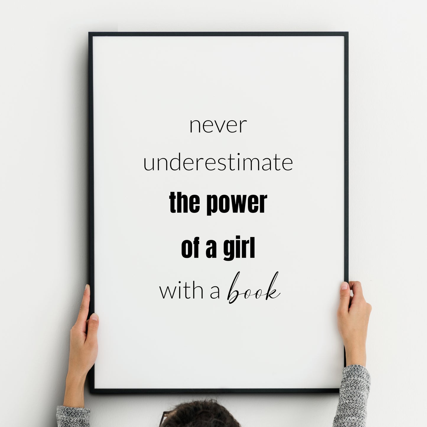 Single monochrome portrait typography print. Text reads: Never underestimate the power of a girl with a book. Text is in a lower case sans serif font. "The power of a girl" is highlighted in bold and "book" is in a script font.