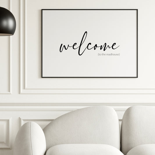 Single landscape typography print. Text reads: welcome (to the madhouse). The word welcome is positioned prominently in a modern script font. Remaining text is in a small, lightweight sans serif font, aligned to the bottom-right of the word welcome. All text is lower case, black on a white background. Styling is elegant and minimalist.