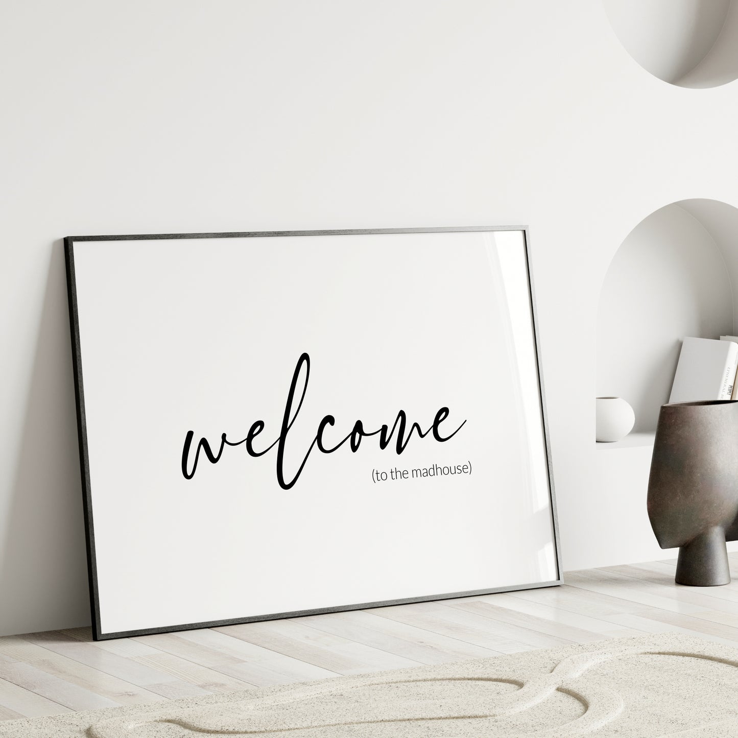 Single landscape typography print. Text reads: welcome (to the madhouse). The word welcome is positioned prominently in a modern script font. Remaining text is in a small, lightweight sans serif font, aligned to the bottom-right of the word welcome. All text is lower case, black on a white background. Styling is elegant and minimalist.