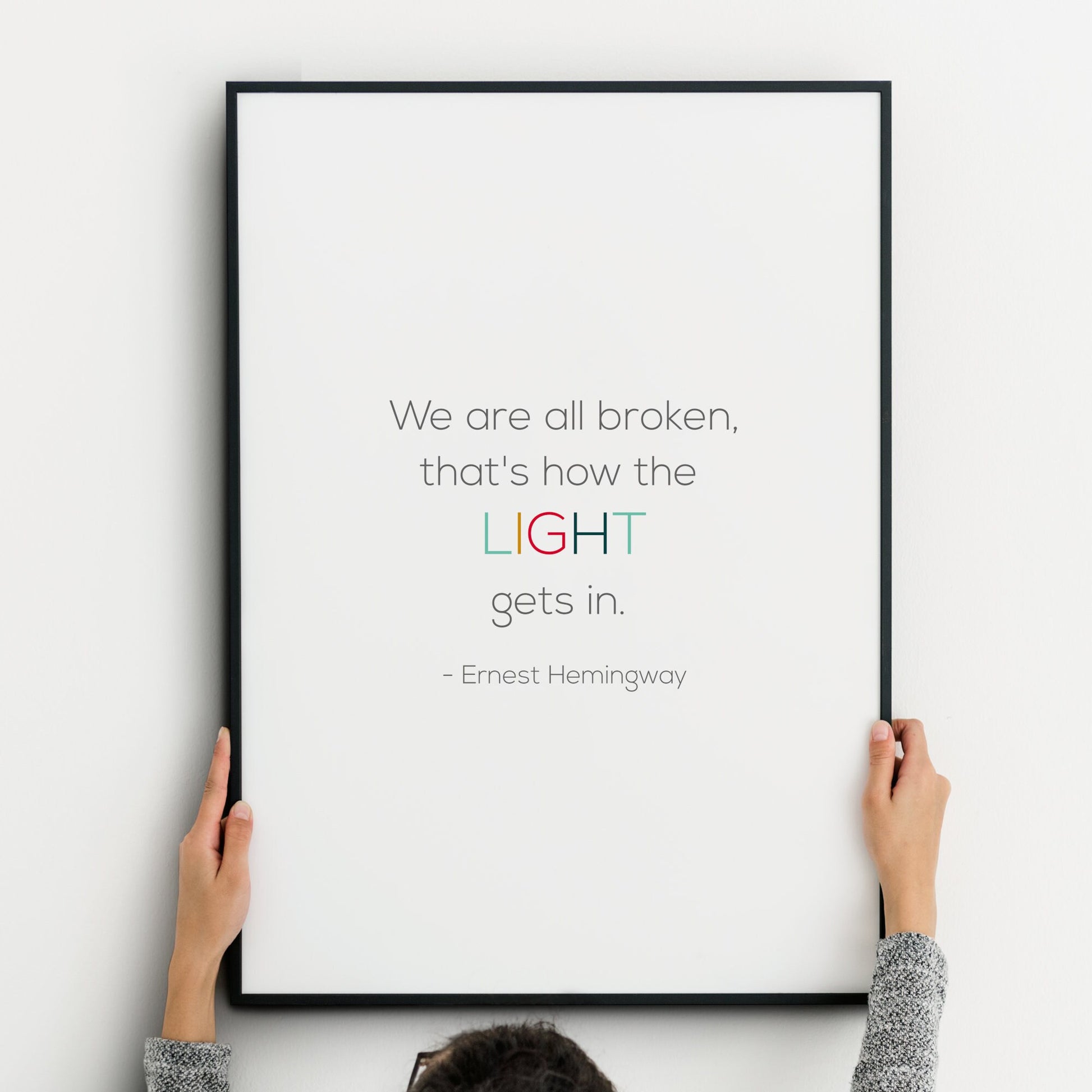 Single portrait typography print. Text reads "We are all broken, that's how the light gets in. - Ernest Hemingway". The word "light" is highlighted in multicolour and upper case. Remaining text is dark grey. Background is white. All text is in a modern sans serif font.