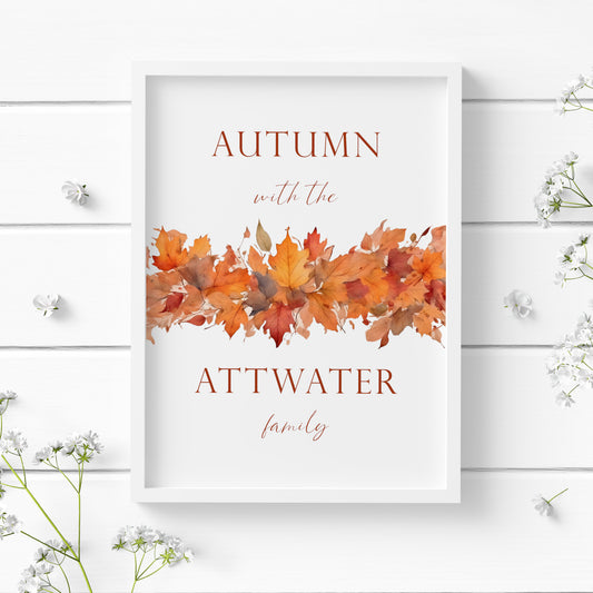 Personalised autumn-themed print. Text reads: Autumn with the <insert family name> family. An illustration of autumn leaves spans the middle of the print, with the text split half above and half below. Text and imagery are in warm autumn tones.