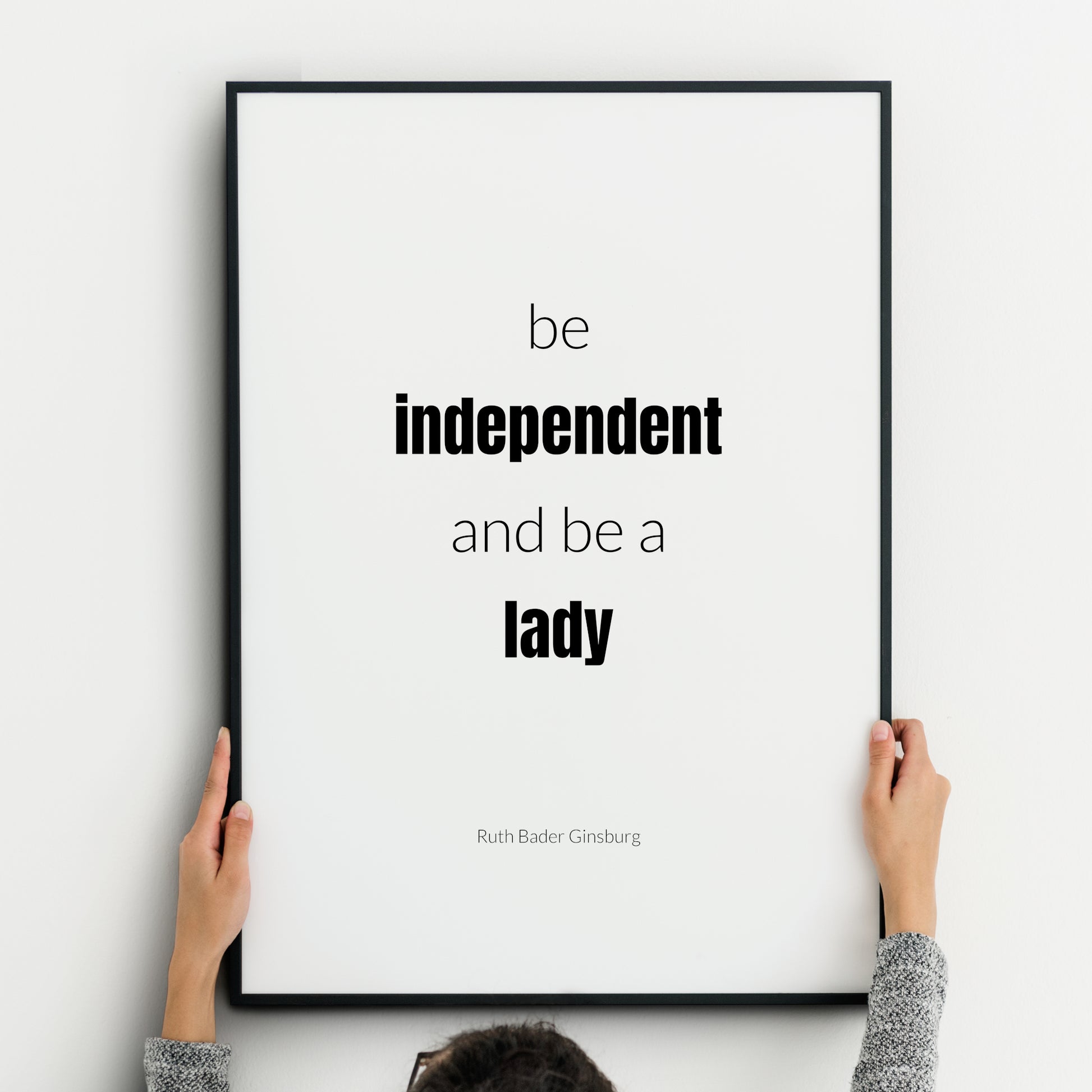 Single portrait typography print. Text reads: Be independent and be a lady. An attribution to Ruth Bader Ginsburg is below. "Independent lady" is highlighted in bold. Text is in a lower case sans serif font, black on a white background.