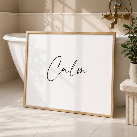 Single landscape print shown in a wooden frame in a bedroom setting. Black text on a white background sees the word "Calm" displayed prominently in an elegant script font.