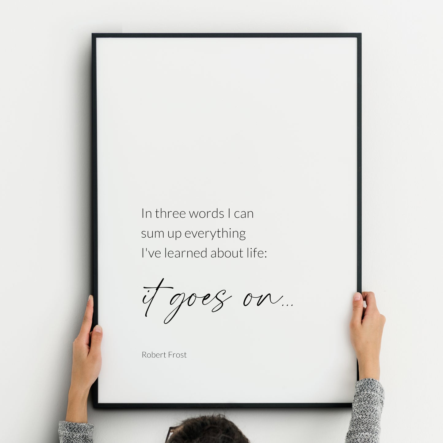 Single portrait typography print featuring a quote from Robert Frost. Text reads: In three words I can sum up everything I’ve learned about life: it goes on… Text is in a lightweight sans serif font, with the exception of the words "it goes on...", which are emphasised in a larger, modern script font. Text is black on a white background. Styling is elegant and minimalist.
