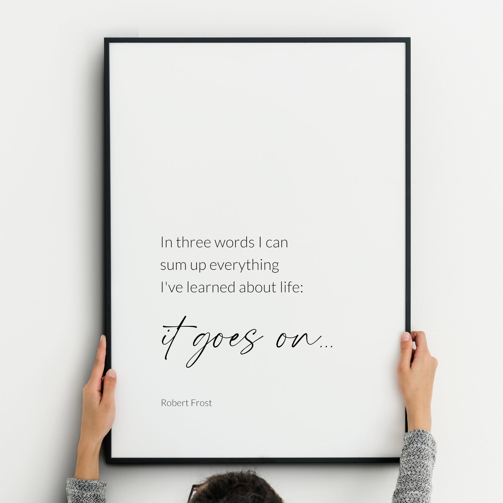Single portrait typography print featuring a quote from Robert Frost. Text reads: In three words I can sum up everything I’ve learned about life: it goes on… Text is in a lightweight sans serif font, with the exception of the words "it goes on...", which are emphasised in a larger, modern script font. Text is black on a white background. Styling is elegant and minimalist.
