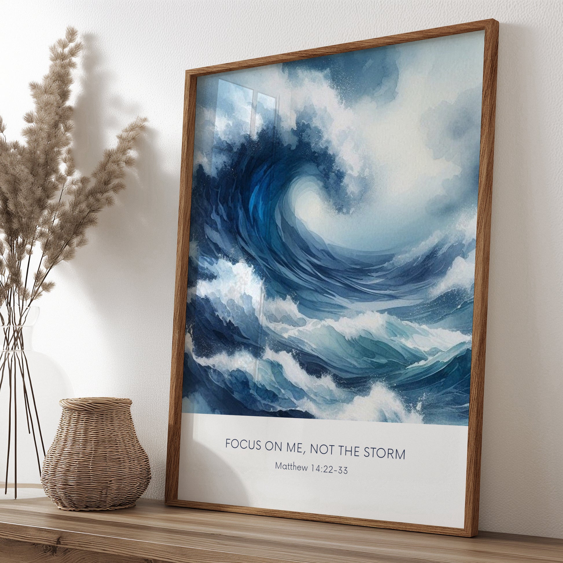 Single portrait illustrated print. Illustration is of a stormy sea showing a large crashing way in moody shades of blue and white. A bible verse is positioned below, reading: Focus on me, not the storm. An attribution to Matthew 14:22-33 is positioned below that again. All text is centre-aligned and in a sans serif font. Text is dark blue on a white background. Styling is contemporary and elegant.