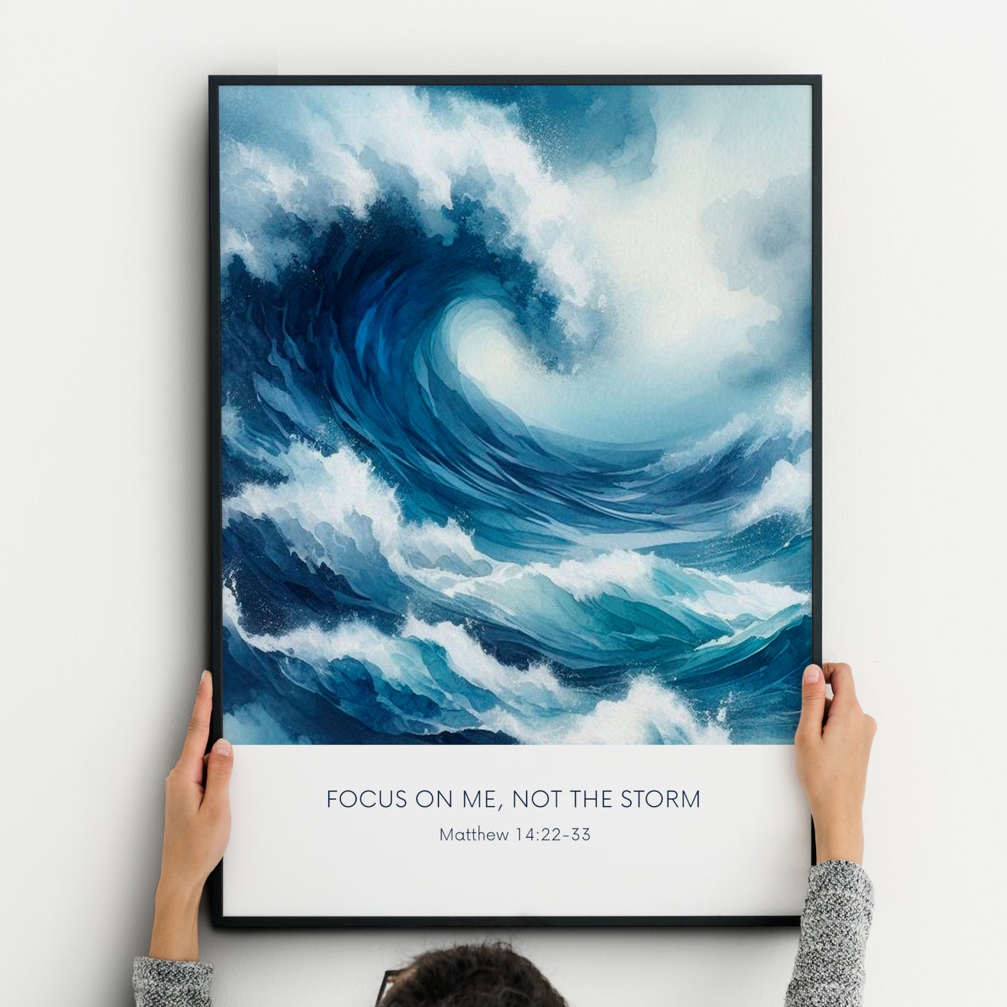 Single portrait illustrated print. Illustration is of a stormy sea showing a large crashing way in moody shades of blue and white. A bible verse is positioned below, reading: Focus on me, not the storm. An attribution to Matthew 14:22-33 is positioned below that again. All text is centre-aligned and in a sans serif font. Text is dark blue on a white background. Styling is contemporary and elegant.
