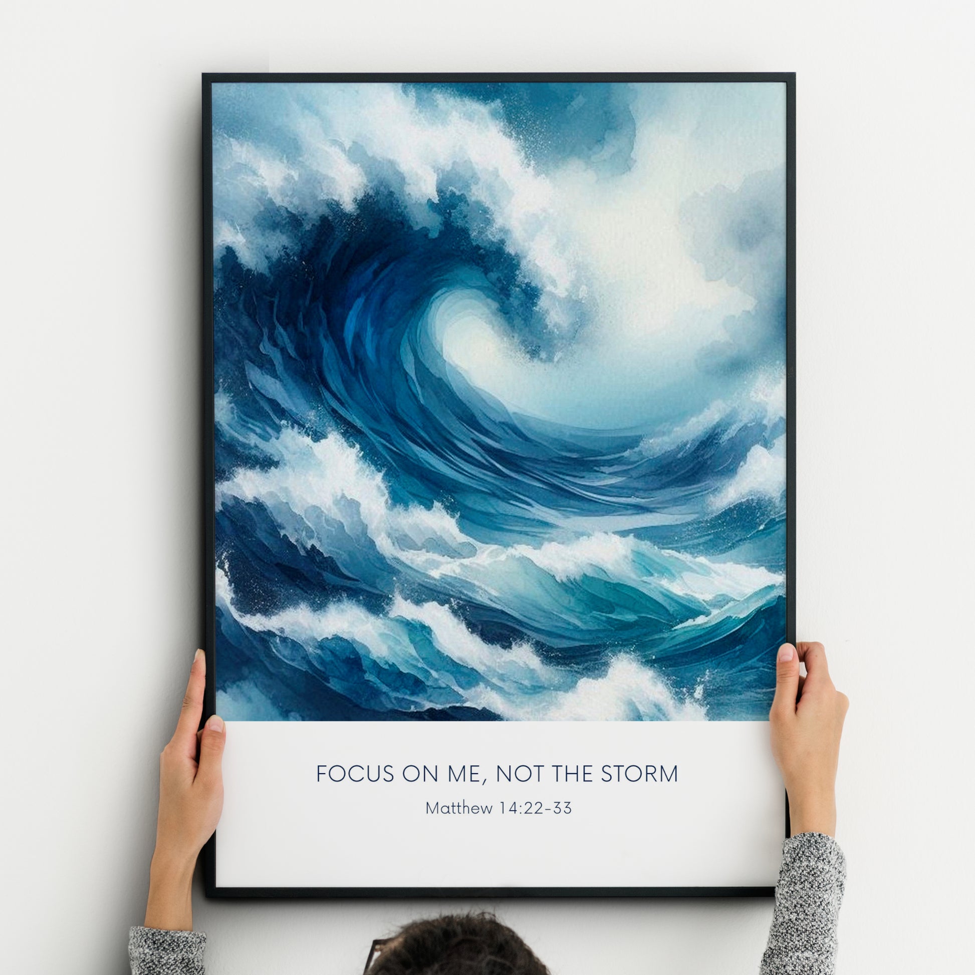 Single portrait illustrated print. Illustration is of a stormy sea showing a large crashing way in moody shades of blue and white. A bible verse is positioned below, reading: Focus on me, not the storm. An attribution to Matthew 14:22-33 is positioned below that again. All text is centre-aligned and in a sans serif font. Text is dark blue on a white background. Styling is contemporary and elegant.