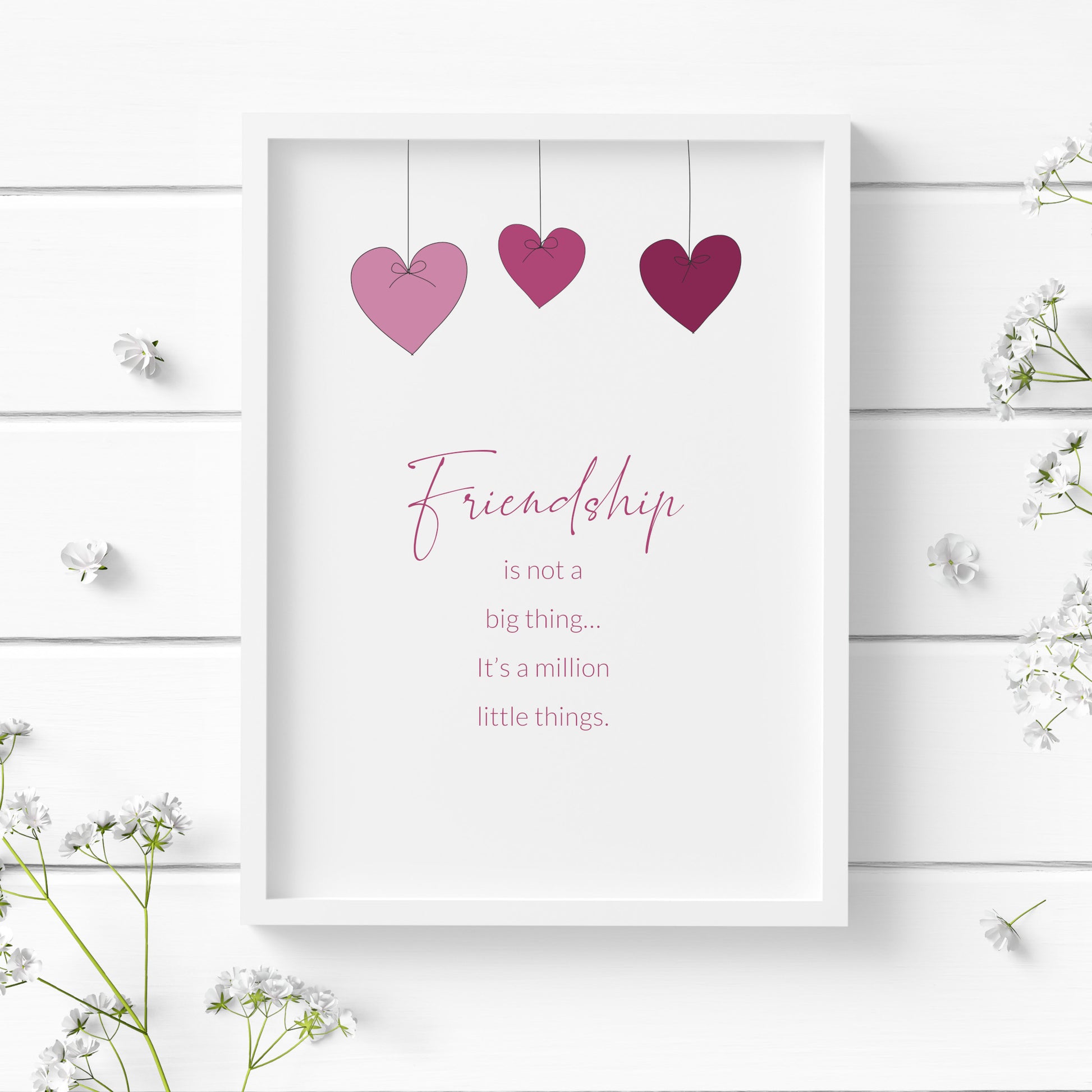 Portrait typography print, reading: Friendship is not a big thing, it's a million little things. The word friendship is placed prominently in a script font. Text is pink on a white background. Images of 3 heart-shaped baubles hang from the top.