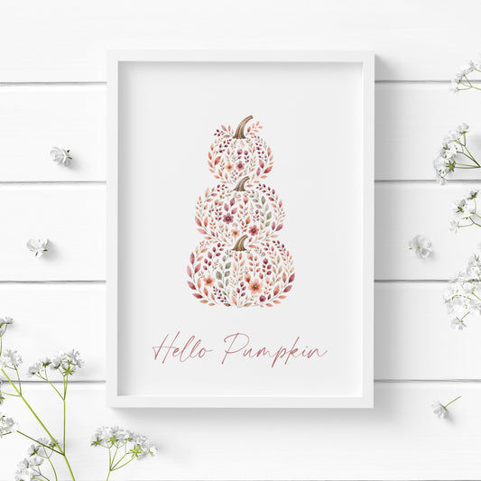 Single portrait illustrated typography print featuring the text "Hello Pumpkin" below a stack of three pumkpins. Text and illustration are in warm autumnal tones with text in a contemporary script font. Styling is cosy cottagecore.