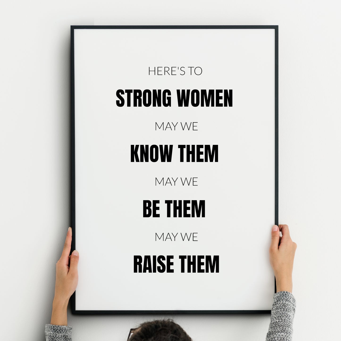 Single portrait typography print. Text reads: Here's to strong women, may we know them, may we be them, may we raise them. All text is in an upper case sans serif font, centre-aligned. Alternate rows are highlighted in bold, including the phrases strong women, know them, be them, raise them. Text is black on a white background. Styling is modern, minimalist and creates a statement.