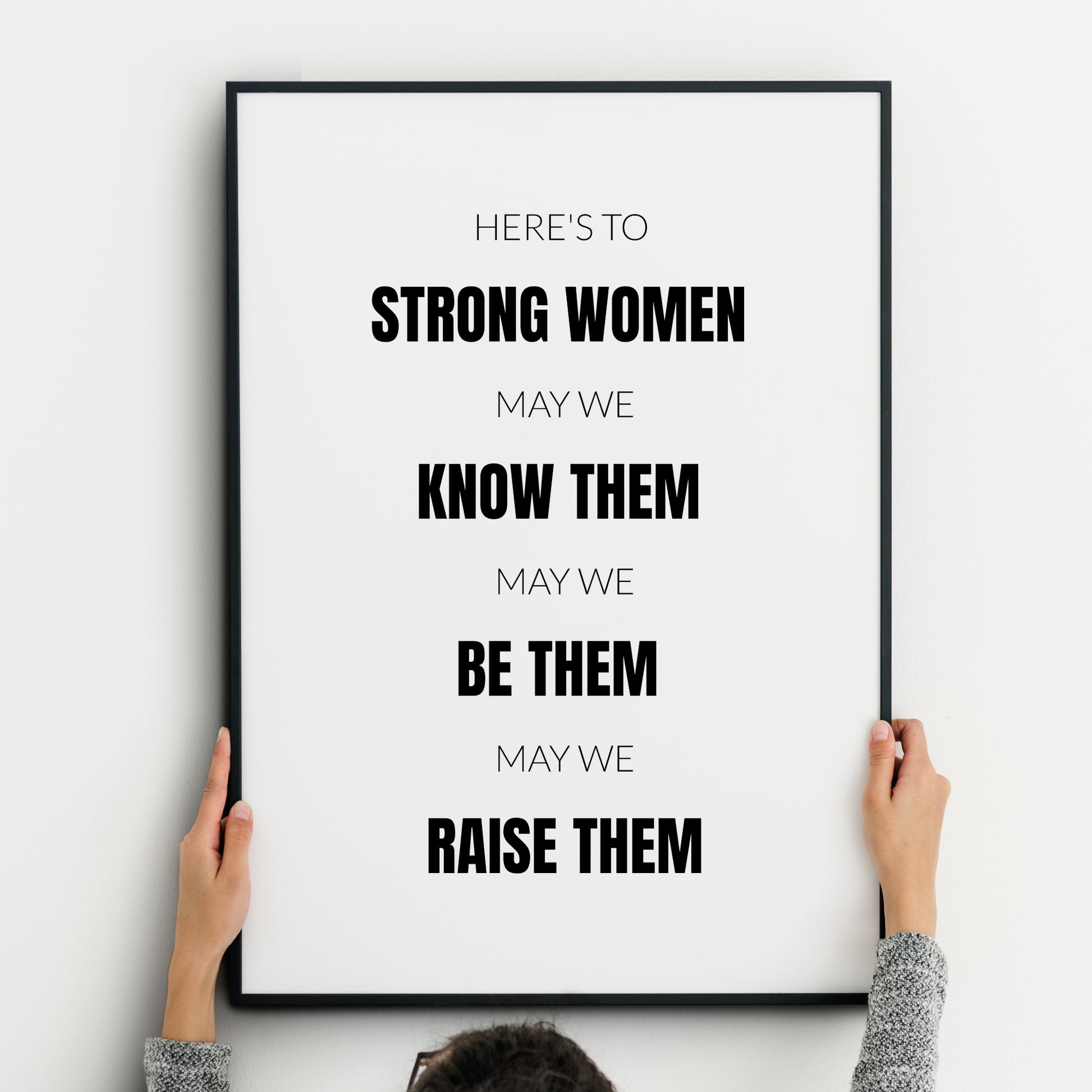 Single portrait typography print. Text reads: Here's to strong women, may we know them, may we be them, may we raise them. All text is in an upper case sans serif font, centre-aligned. Alternate rows are highlighted in bold, including the phrases strong women, know them, be them, raise them. Text is black on a white background. Styling is modern, minimalist and creates a statement.