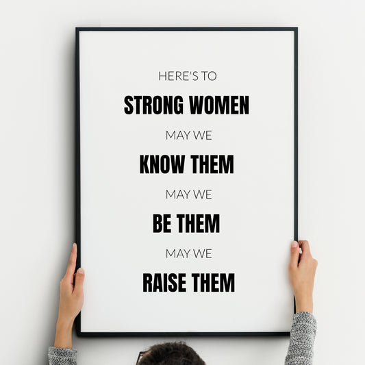 Single portrait typography print. Text reads: Here's to strong women, may we know them, may we be them, may we raise them. All text is in an upper case sans serif font, centre-aligned. Alternate rows are highlighted in bold, including the phrases strong women, know them, be them, raise them. Text is black on a white background. Styling is modern, minimalist and creates a statement.