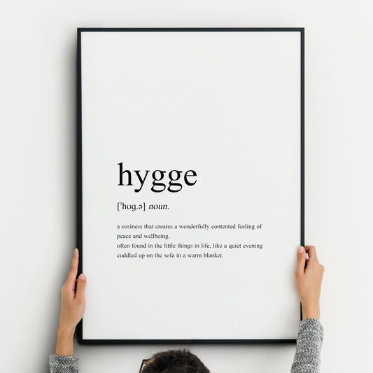 Single portrait typography print featuring a dictionary-style definition of the word hygge. It includes the word itself, pronunciation, type and definition. Text is in a lower case serif font, left-aligned and black on a white background.