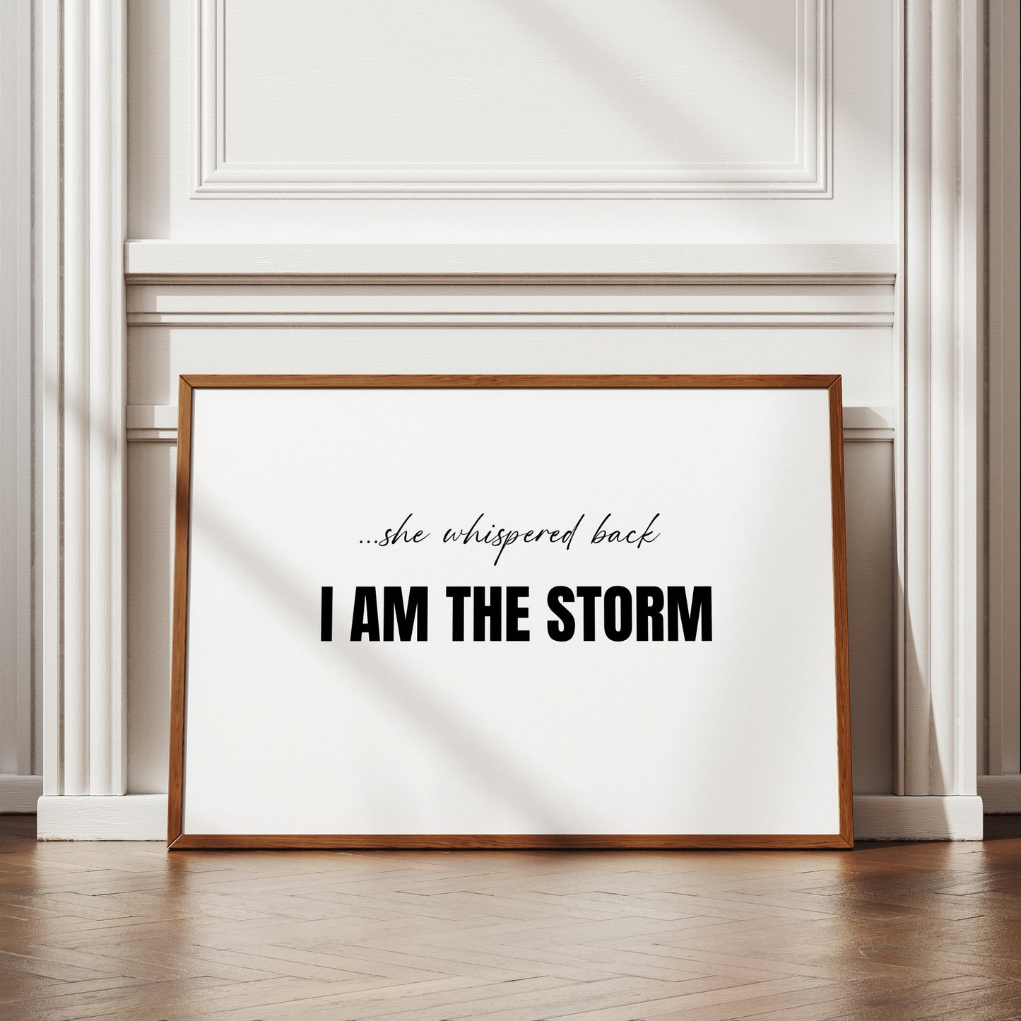 Single landscape typography print. Text reads: ...she whispered back I am the storm. The initial text is in a feminine script font, with "I am the storm" in a bold upper case sans serif font. All text is centre-aligned, black on a white background. Styling is modern and minimalist.