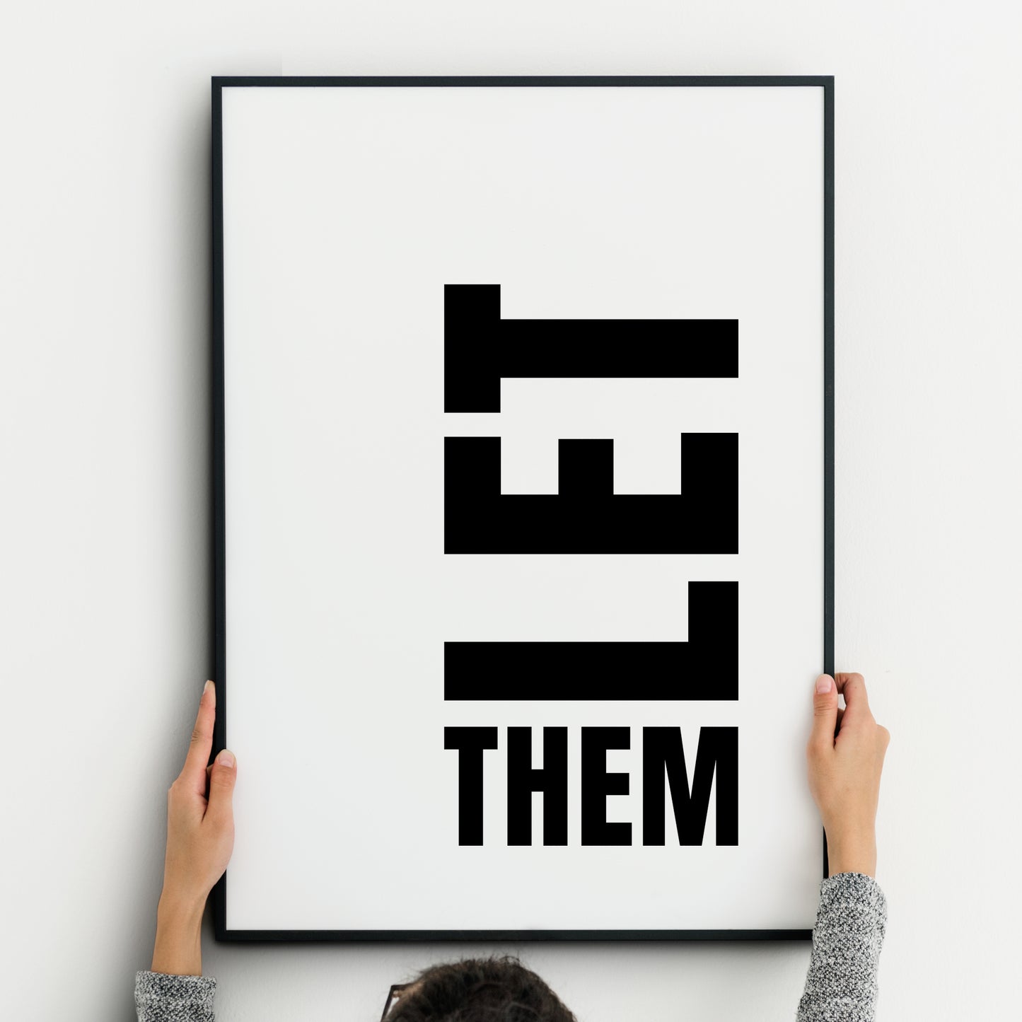 Minimalist black-and-white typography print featuring the phrase ‘LET THEM.’ The word ‘LET’ is displayed vertically in bold, block capital letters, stacked downward, while the word ‘THEM’ appears horizontally beneath in the same bold uppercase font. Clean white background with strong graphic contrast, modern and impactful design.