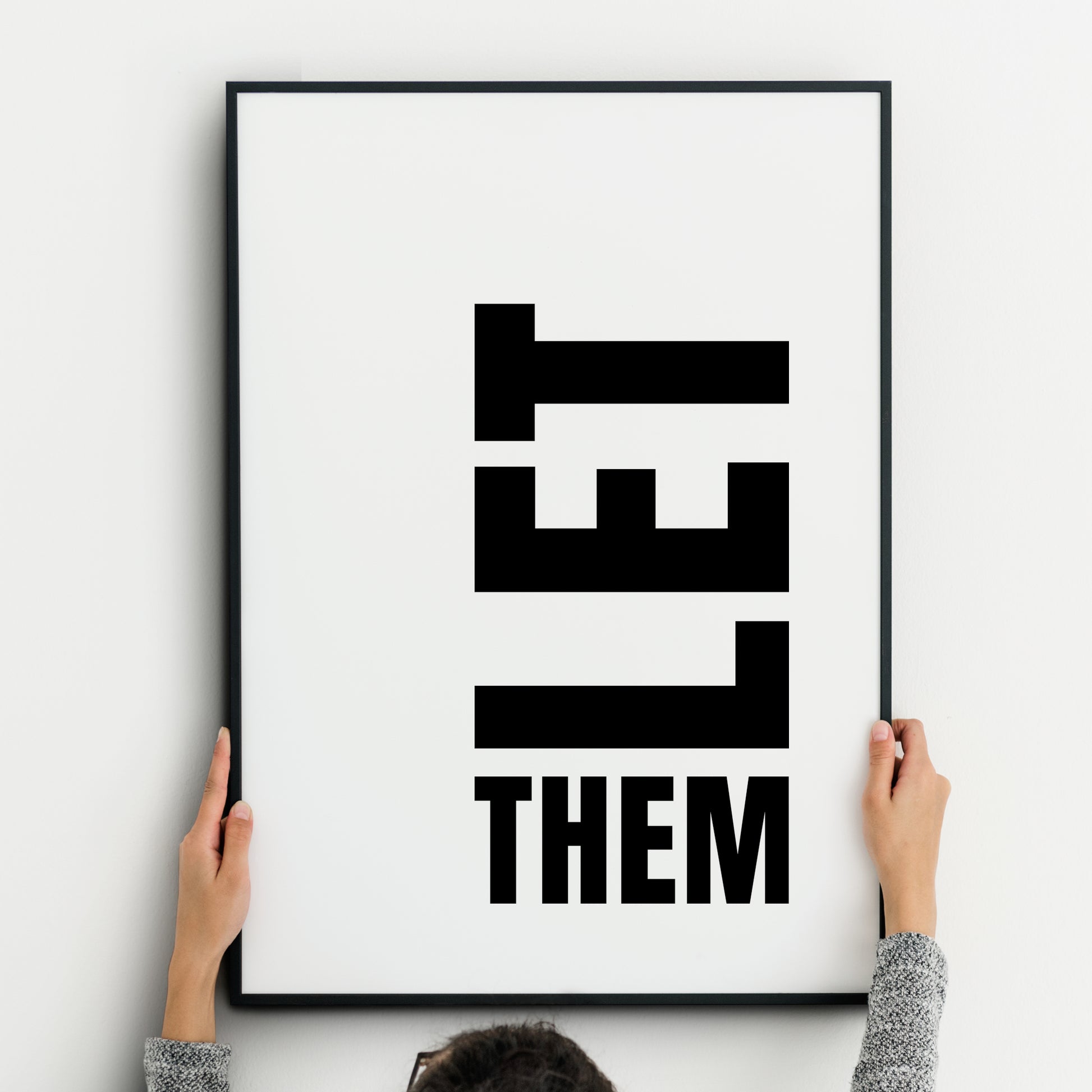 Minimalist black-and-white typography print featuring the phrase ‘LET THEM.’ The word ‘LET’ is displayed vertically in bold, block capital letters, stacked downward, while the word ‘THEM’ appears horizontally beneath in the same bold uppercase font. Clean white background with strong graphic contrast, modern and impactful design.