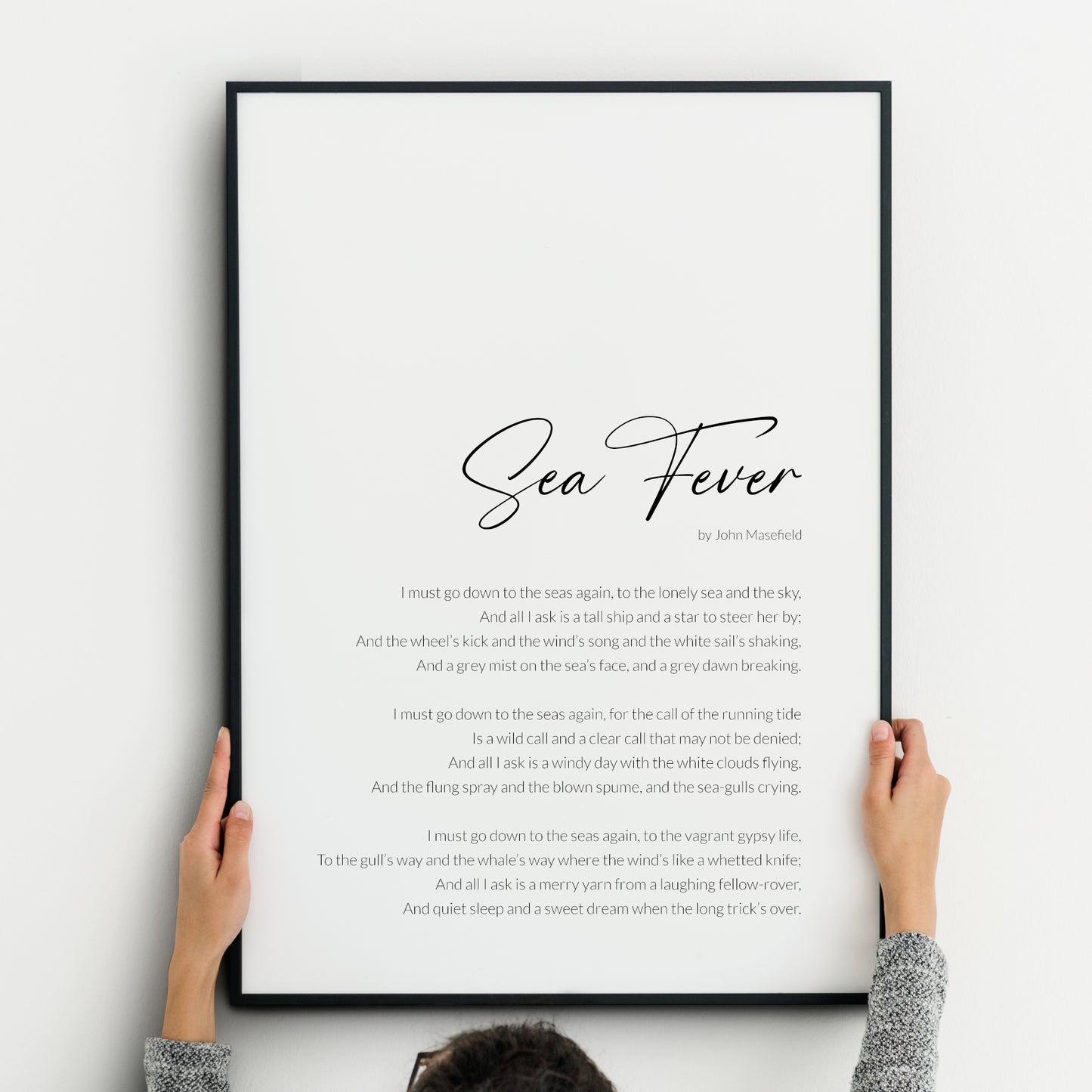 Minimalist black-and-white typography print featuring the poem Sea Fever by John Masefield. The title is written in an elegant, swirling script that echoes the movement of the sea, with the body text in a lightweight sans serif font. The poem is positioned to the bottom right of the piece with a slim margin.