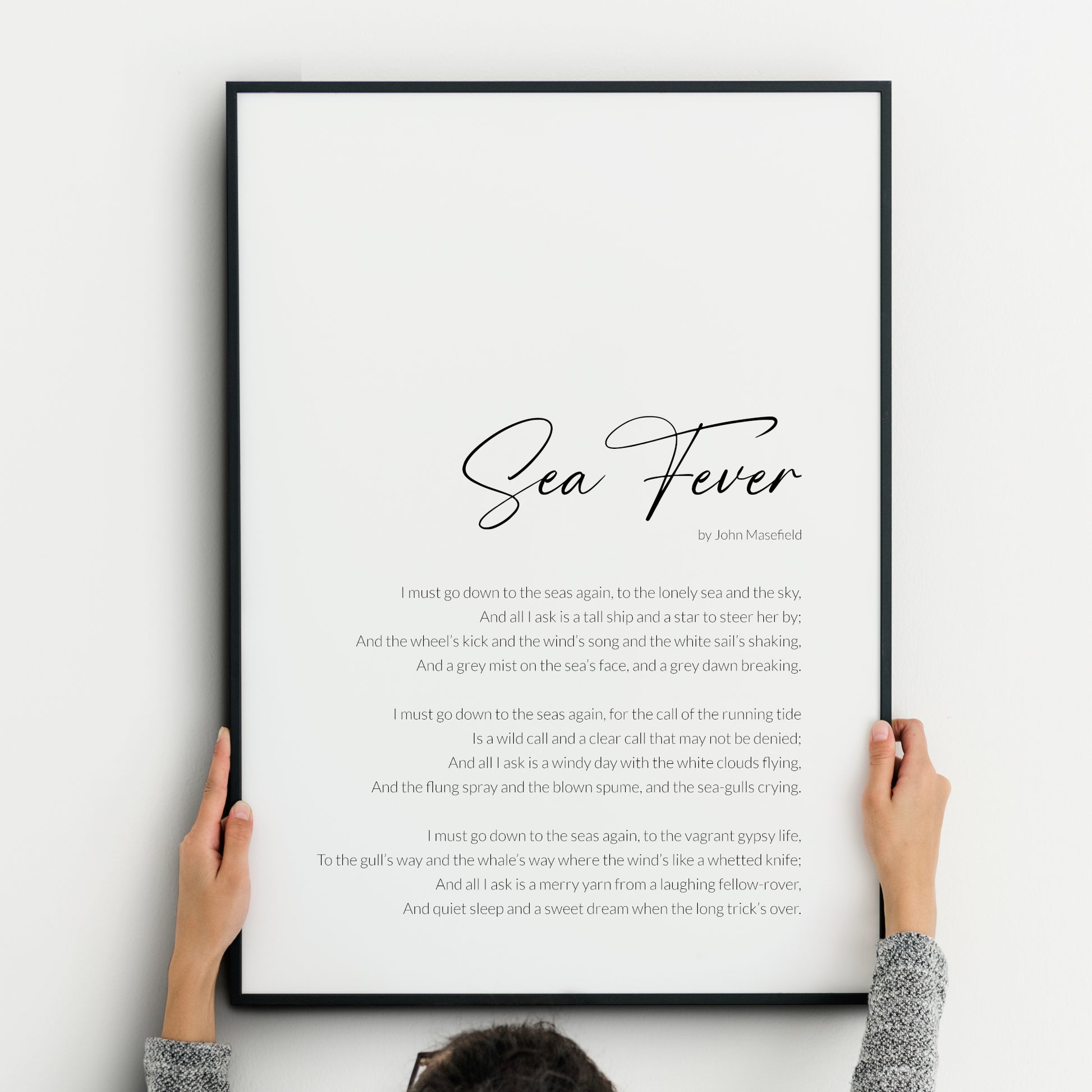 Minimalist black-and-white typography print featuring the poem Sea Fever by John Masefield. The title is written in an elegant, swirling script that echoes the movement of the sea, with the body text in a lightweight sans serif font. The poem is positioned to the bottom right of the piece with a slim margin.