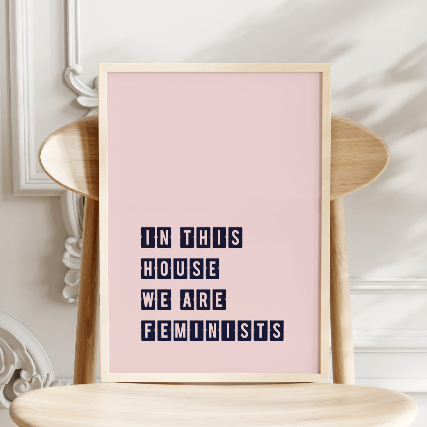 Single portrait typography print. Text read: In this house we are feminists. Text is in a boxed font in upper case. Text is dark blue on a pale pink background. Styling is contemporary and edgy.
