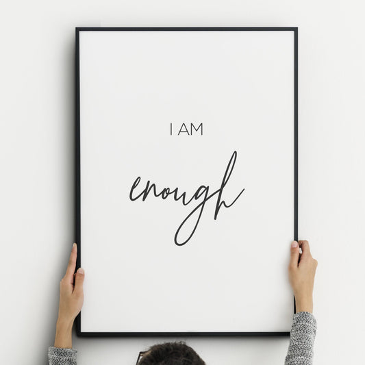Single portrait print displayed in a black frame. Its minimalist style shows black text on a white background with text that reads I am enough. The word enough is displayed prominently in an elegant script font.