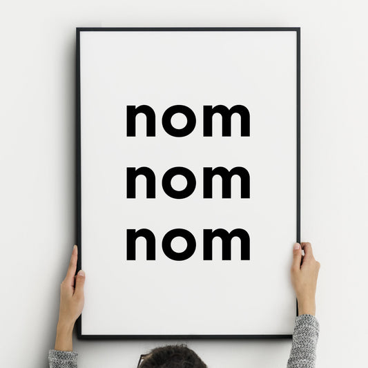 Single portrait typography print featuring the quote "nom nom nom". The words are stacked vertically in a bold lower case sans serif font. The styling is edgy and contemporary. Text is black on a white background.