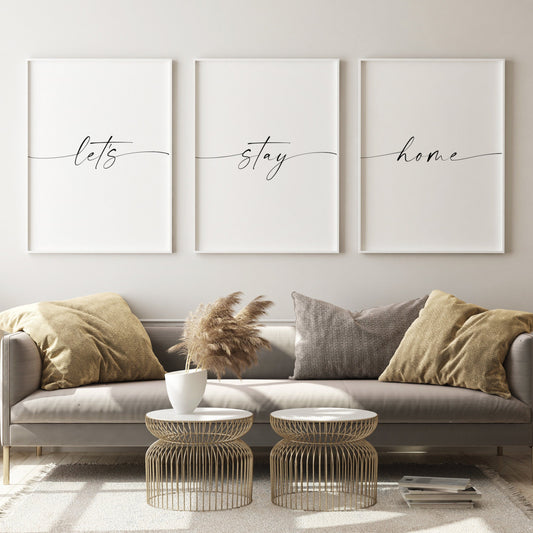Set of 3 portrait typography posters shown side by side in a living room setting. Text reads: let's stay home. There is one word on each print, with the first and last characters of each trailing out to the edges of the respective print.