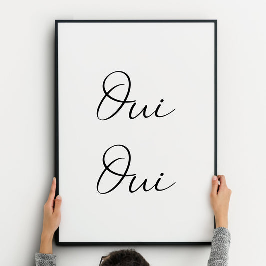 A minimalist black and white wall art print featuring the French words ‘Oui Oui’ displayed across two lines. Text is written in an elegant, flowing script, centred both horizontally and vertically. The typography stands out against a clean white background for a simple, sophisticated look.