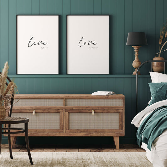 Set of 2 portrait typography prints. Print 1 text reads: Live by the sun. Print 2 text reads: Love by the moon. The words live and love are positioned prominently in an elegant script font, with the remaining text on each in a crisp sans serif font.